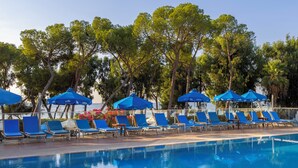 A poolside area with lounge chairs and umbrellas, surrounded by trees. - Park Beach Hotel (Limassol)
