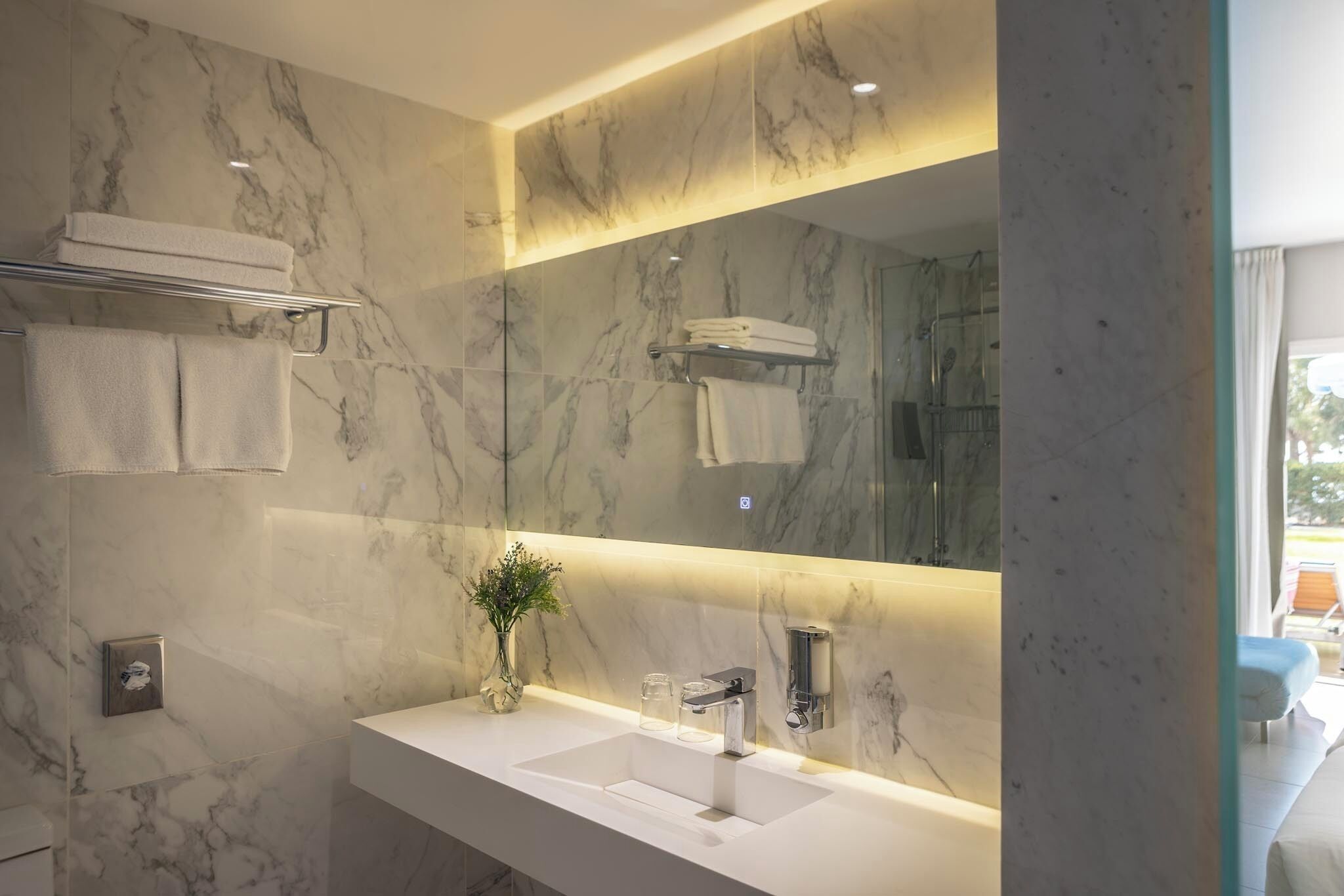 Une salle de bain moderne avec un pare-baignoire en marbre, un grand miroir, un lavabo blanc et un porte-serviettes.
