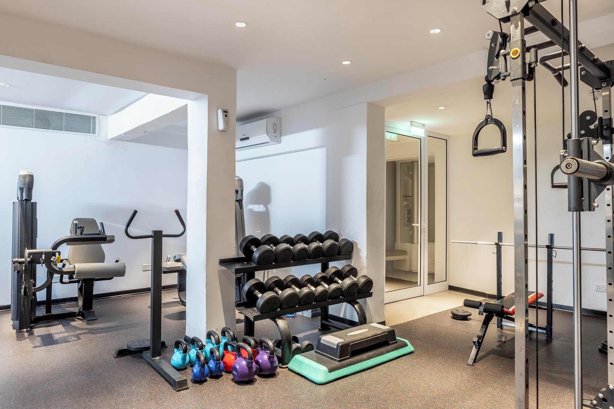 A modern gym with various exercise equipment, including dumbbells, kettlebells, and a squat rack.