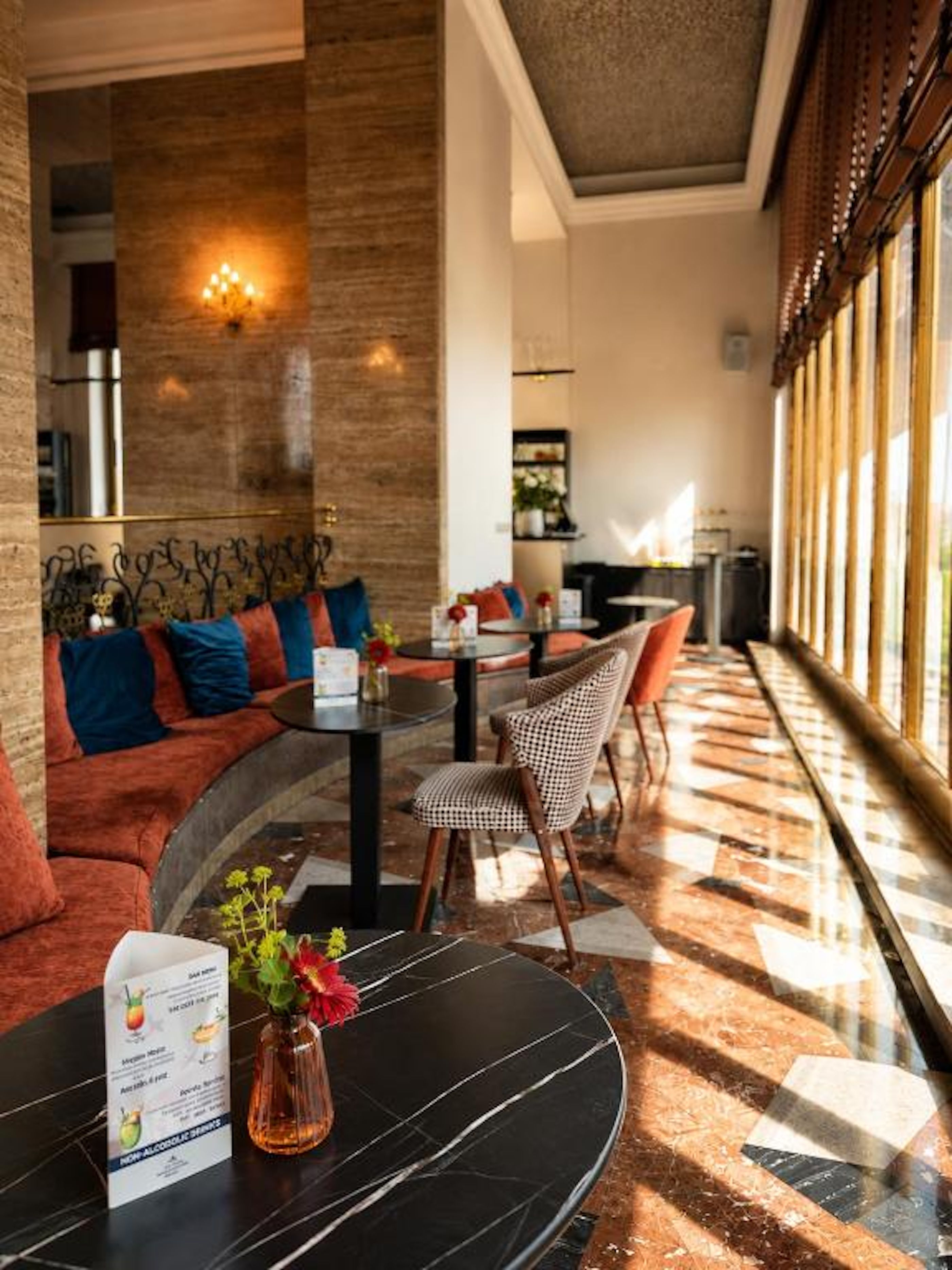 Un hall d’hôtel comprenant un espace salon, une table avec un menu et une grande fenêtre laissant entrer la lumière naturelle.