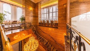 Una imponente escalera con barandillas ornamentadas y un candelabro, que conduce a un balcón con vistas a la ciudad.