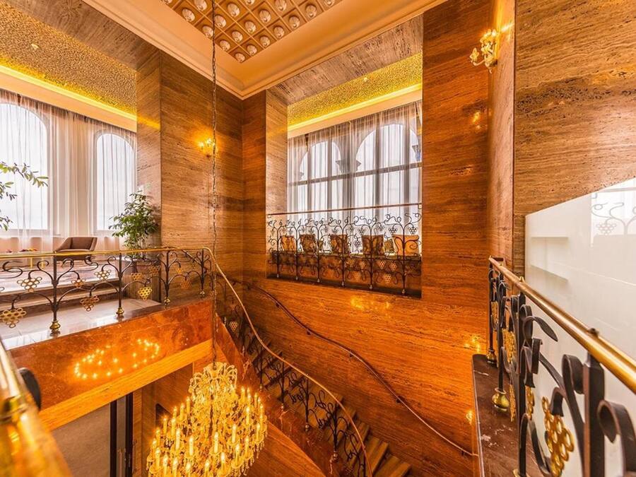 Una imponente escalera con barandillas ornamentadas y un candelabro, que conduce a un balcón con vistas a la ciudad.