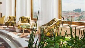 Una habitación amplia con un gran ventanal que ofrece vistas a la ciudad, dos sillones, una mesita y un ventanal de piso a techo con cortinas translúcidas.
