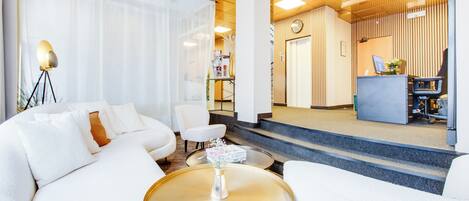 A modern hotel lobby with a white sofa, a round coffee table, and a reception desk.