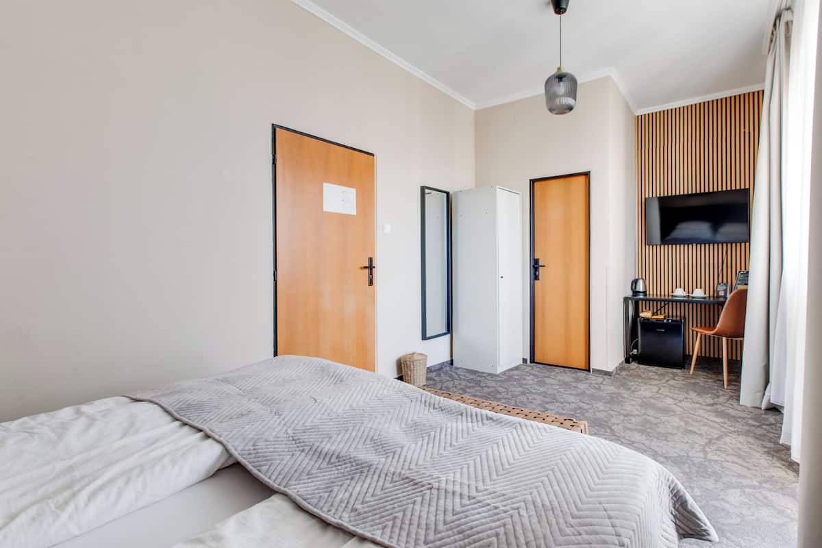A hotel room with a bed, a desk, a chair, and a TV mounted on the wall.