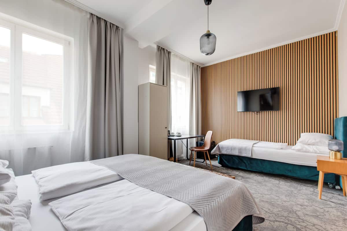 A hotel room with two beds, a desk, a chair, a TV, and a wooden accent wall.