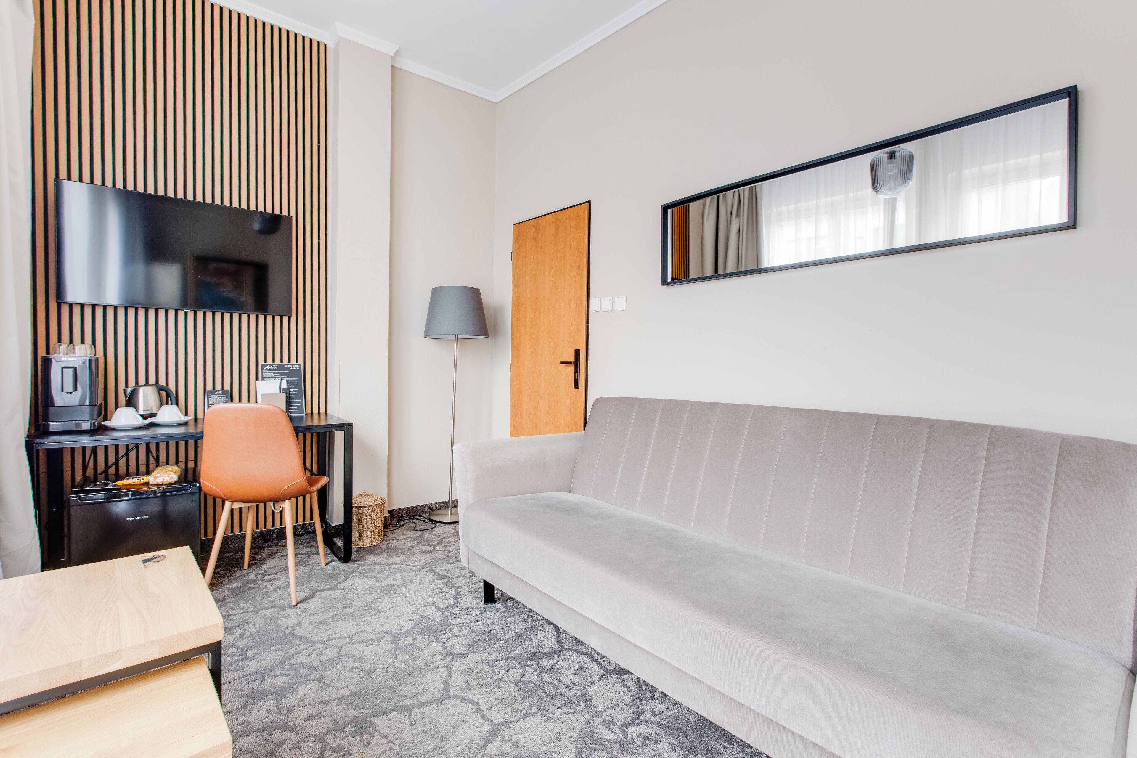Ein modernes Zimmer mit einer Couch, einem Schreibtisch mit Flachbildfernseher, einer Lampe und einer Wandpaneele aus Holz.