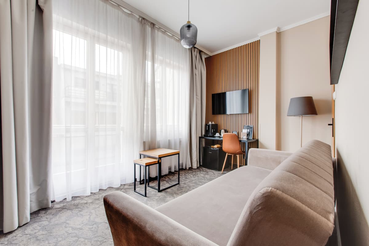 A modern hotel room with a large bed, a desk, a chair, a TV, and a lamp.