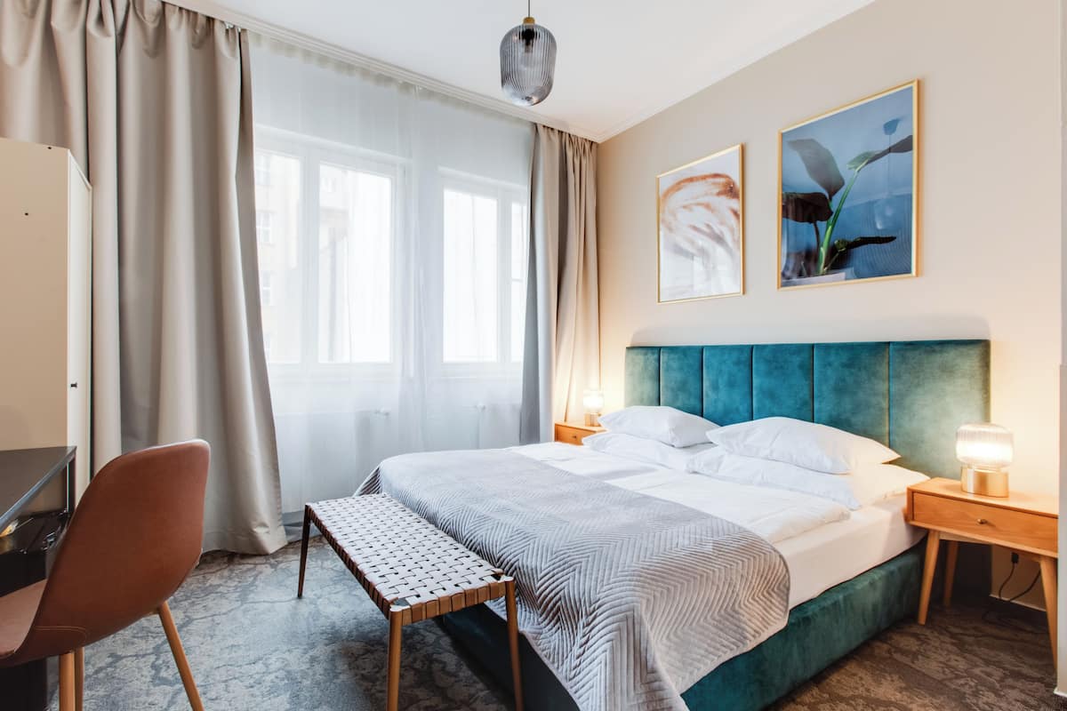 A hotel room with a bed, bedside tables, a desk, a chair, and a bench.