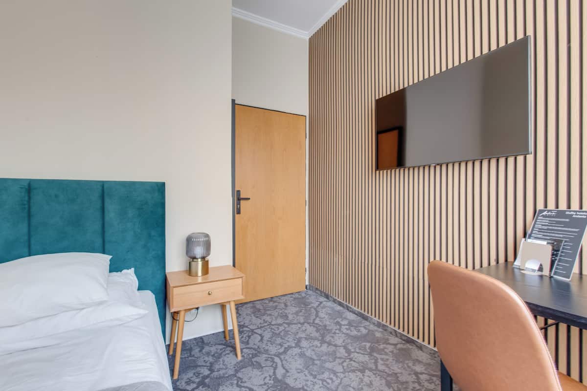 A hotel room with a bed, a desk, a chair, a flat-screen TV, and a wooden panel wall.