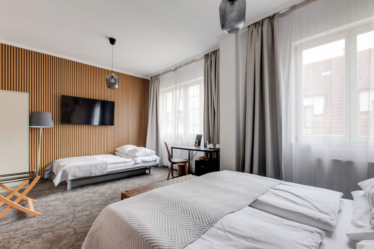 A hotel room with a large bed, a smaller bed, a desk, and a TV mounted on the wall.