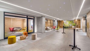 Um lobby moderno com layout espaçoso, com diferentes áreas de estar, uma receção e luz natural proveniente de amplas janelas.