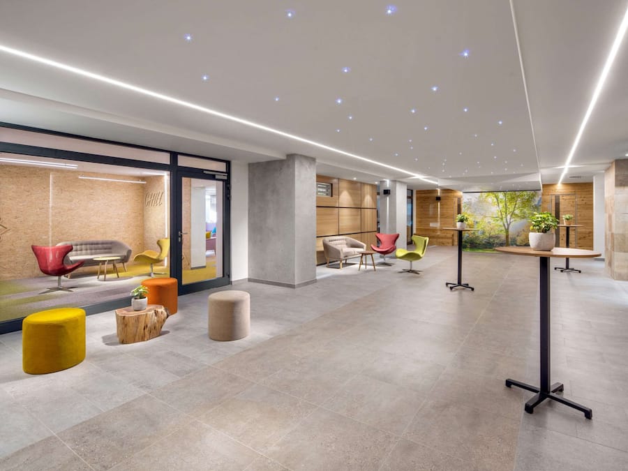 A modern lobby with a spacious layout, featuring a mix of seating areas, a reception desk, and natural light from large windows.