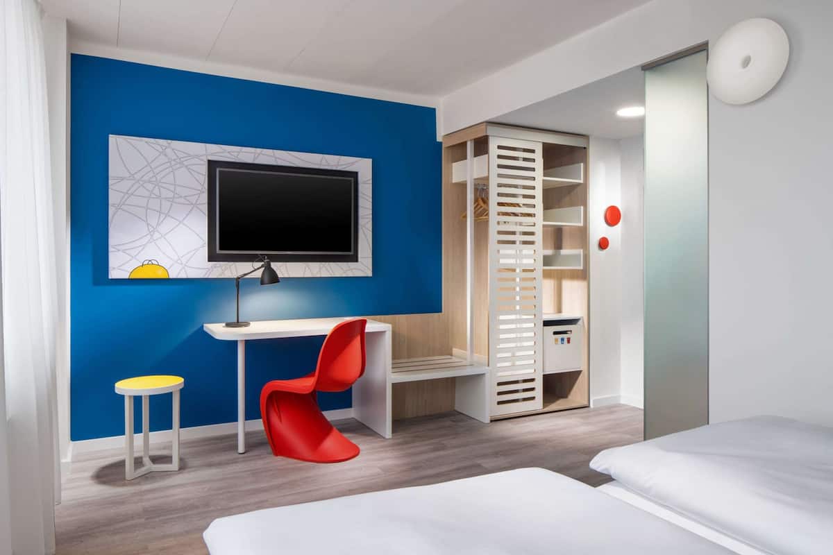 Une chambre moderne avec un mur d’accent bleu, un bureau avec un ordinateur, une chaise rouge, une armoire et un lit.