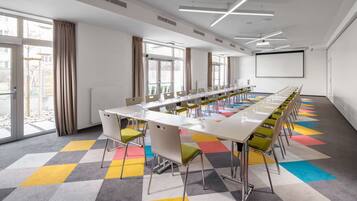 Un salón de conferencias con una larga mesa, sillas, una pantalla de proyector y ventanas amplias.
