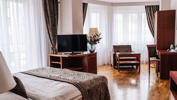 Quarto de hotel com cama, escrivaninha, televisão, poltrona e sofá.