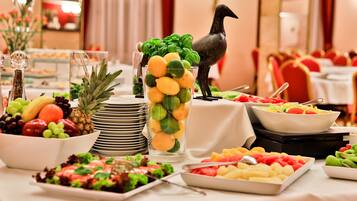 Een buffet met verschillende soorten fruit, salades en een decoratief beeldje van een vogel.
