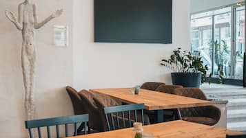 Un interior moderno con una mesa y sillas de madera, una planta grande en maceta y un televisor de pantalla plana montado en la pared.
