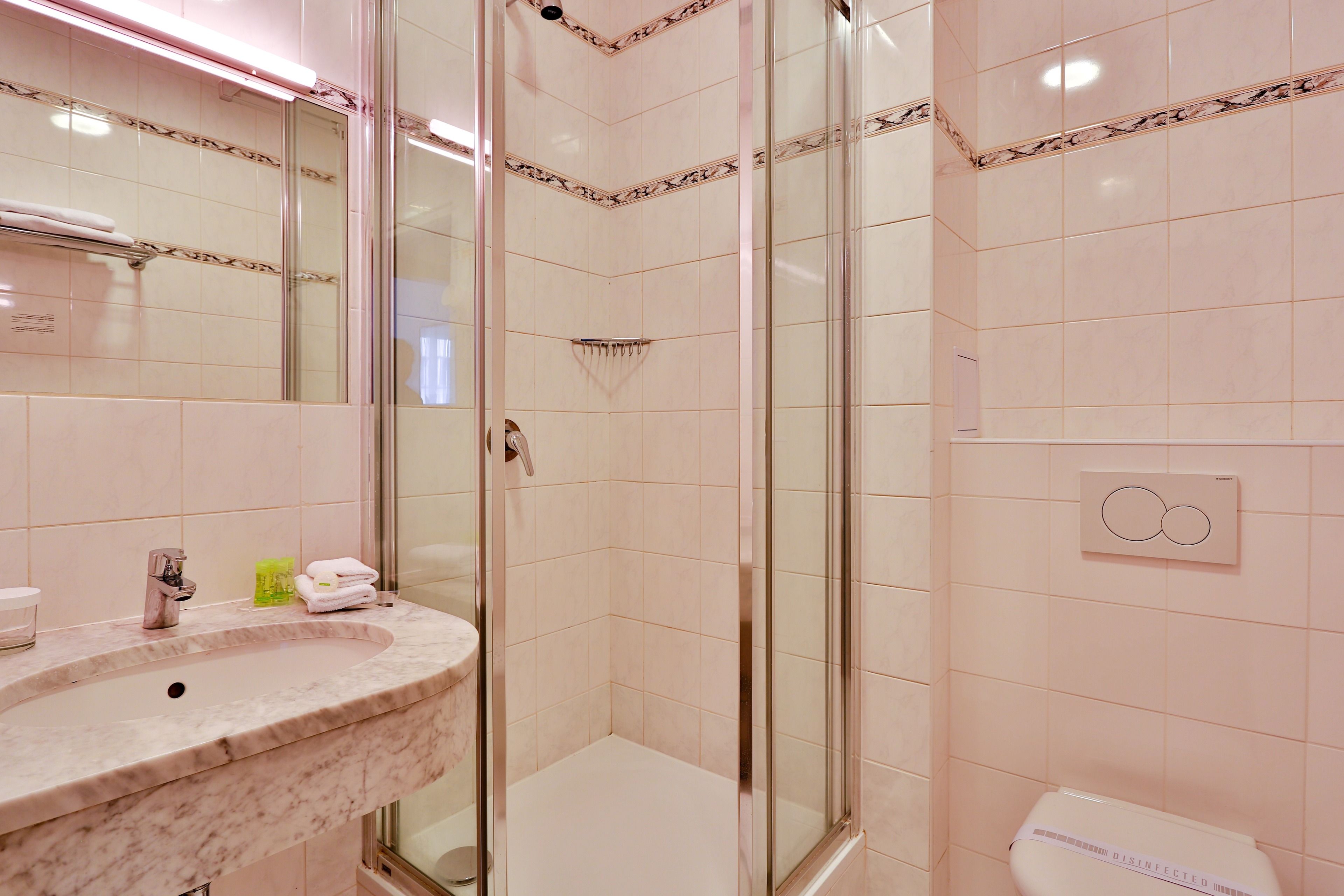 Ein Badezimmer mit Marmorwaschbecken, einer Duschkabine aus Glas und einer Toilette mit Desinfektionshinweis.