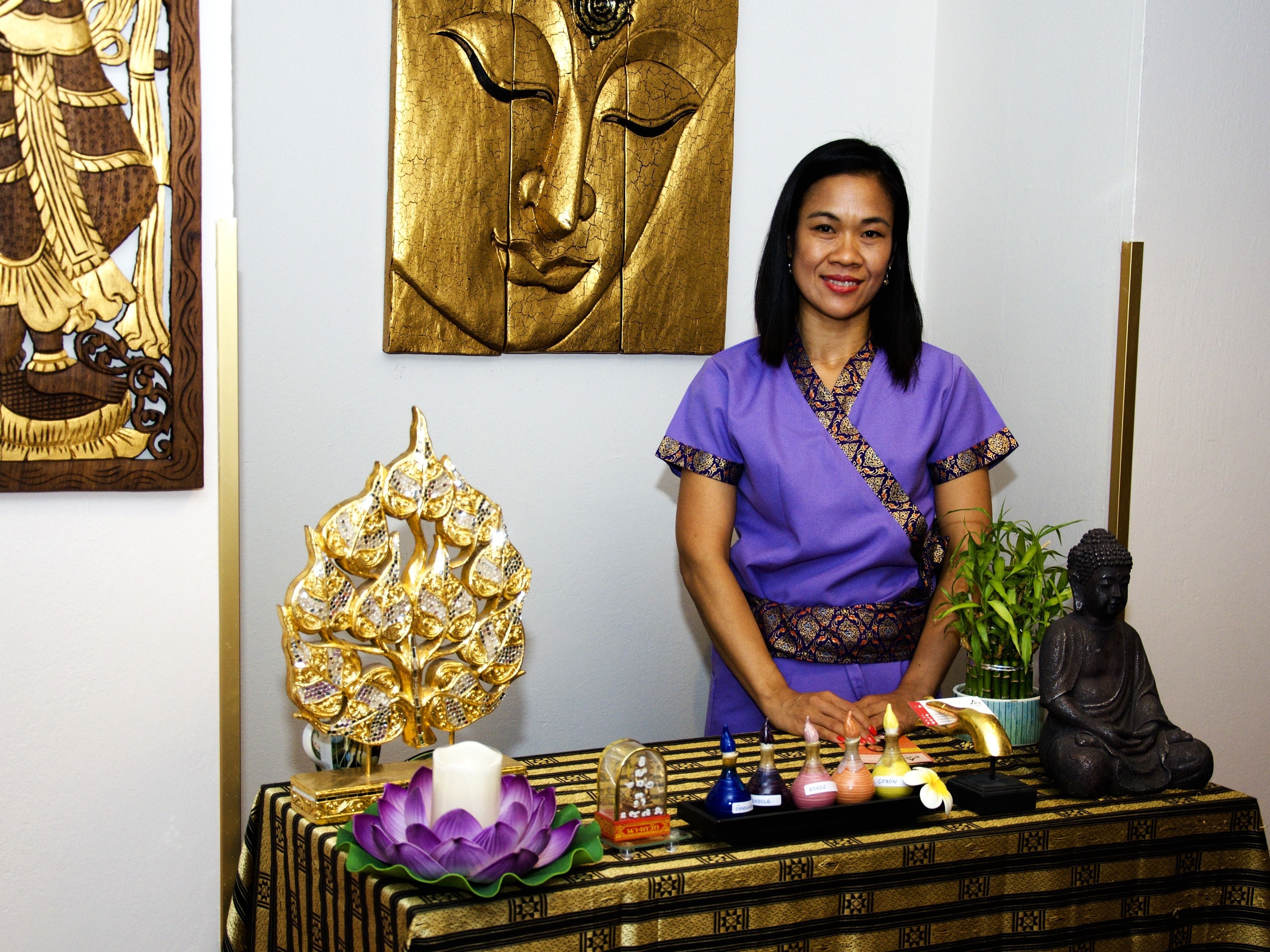 Une personne se tient devant une table sur laquelle se trouvent divers objets, notamment une statue de Bouddha, un objet décoratif doré, ainsi qu’un plateau avec des bougies et des flacons d’encens.