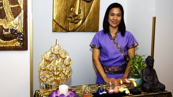 Une personne se tient devant une table sur laquelle se trouvent divers objets, notamment une statue de Bouddha, un objet décoratif doré, ainsi qu’un plateau avec des bougies et des flacons d’encens.