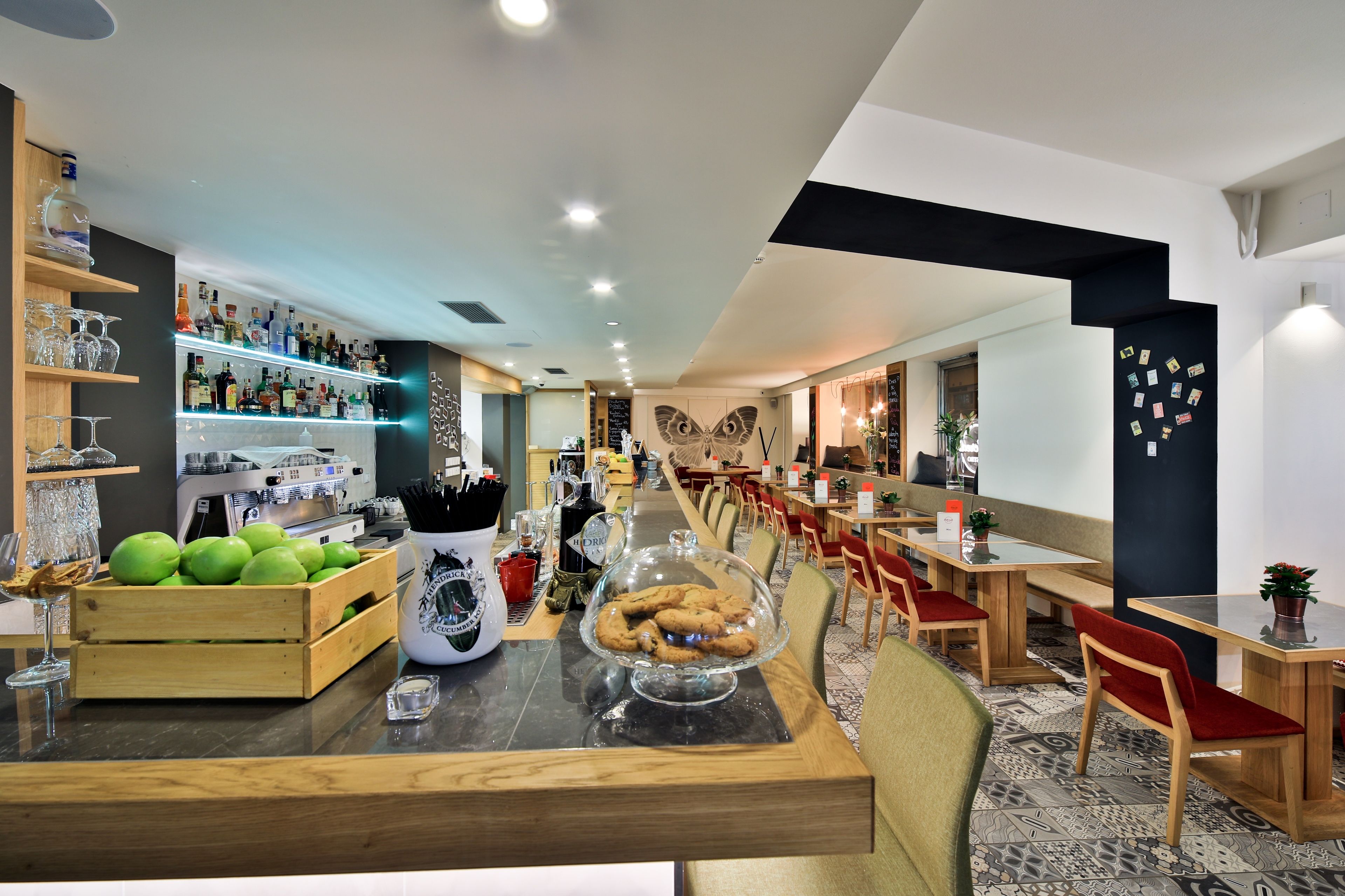 A restaurant with a long counter, wooden chairs, and a variety of bottles on shelves.