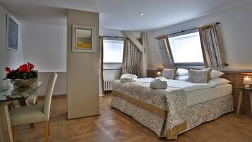 A bedroom with a bed, a bedside table, a mirror, a window with curtains, a radiator, and a dining table with chairs.