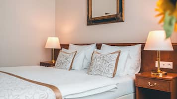 A neatly made bed with white linens and patterned pillows, two bedside lamps, a wooden nightstand, and a mirror on the wall.