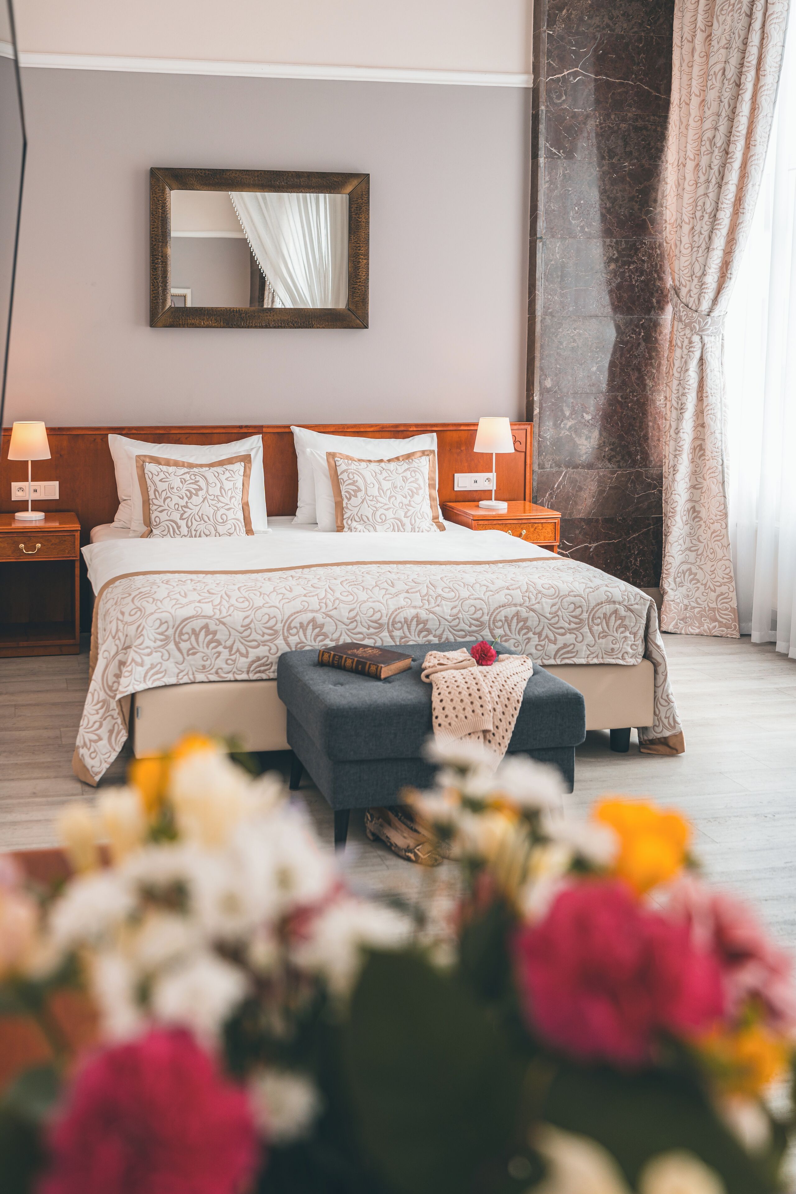 Un dormitorio ordenado con una cama grande, mesitas de noche, un espejo y un banco decorativo.