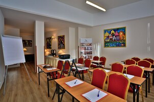 Uma sala de conferência com cadeiras vermelhas, mesas de madeira, um quadro branco e um projetor.