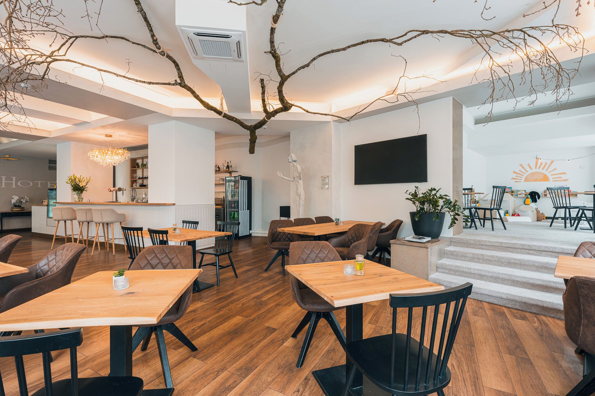Un hall d’hôtel moderne avec un revêtement de sol en bois, un bar et un espace salon avec des tables et des chaises.