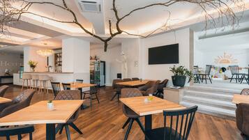 A modern hotel lobby with wooden flooring, a bar area, and a seating area with tables and chairs.