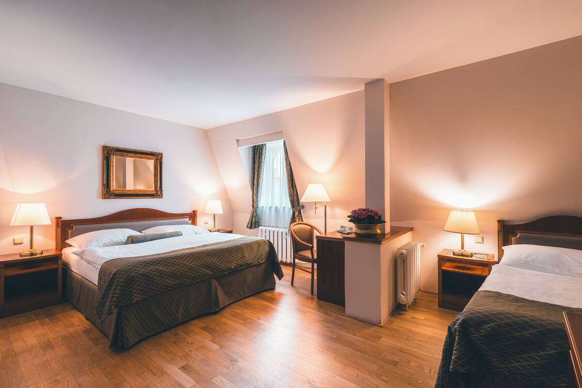 Habitación de hotel con cama doble, dos mesitas de noche con lámparas, una silla, un escritorio pequeño y un radiador.