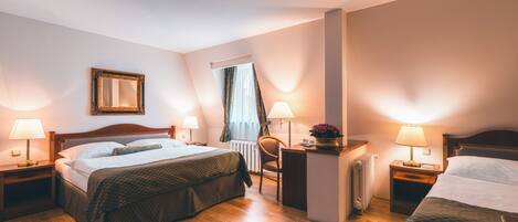 A hotel room with a double bed, two bedside tables with lamps, a chair, a small desk, and a radiator.