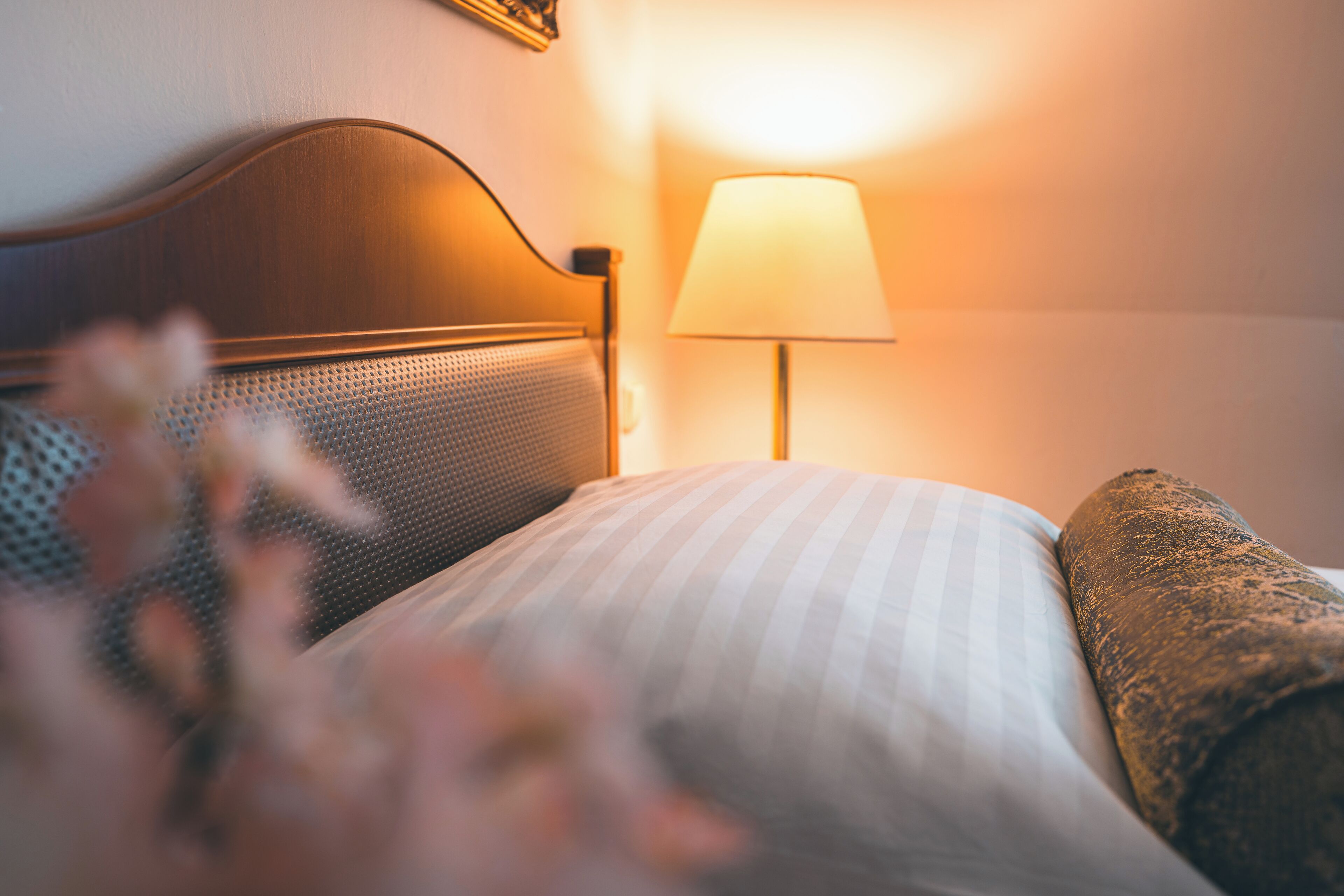 Ein ordentlich bezogenes Bett mit gestreiftem Kopfkissen und einer strukturierten Decke, eine Wandlampe und ein Bilderrahmen an der Wand.