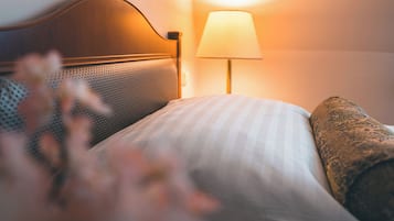 Ein ordentlich bezogenes Bett mit gestreiftem Kopfkissen und einer strukturierten Decke, eine Wandlampe und ein Bilderrahmen an der Wand.