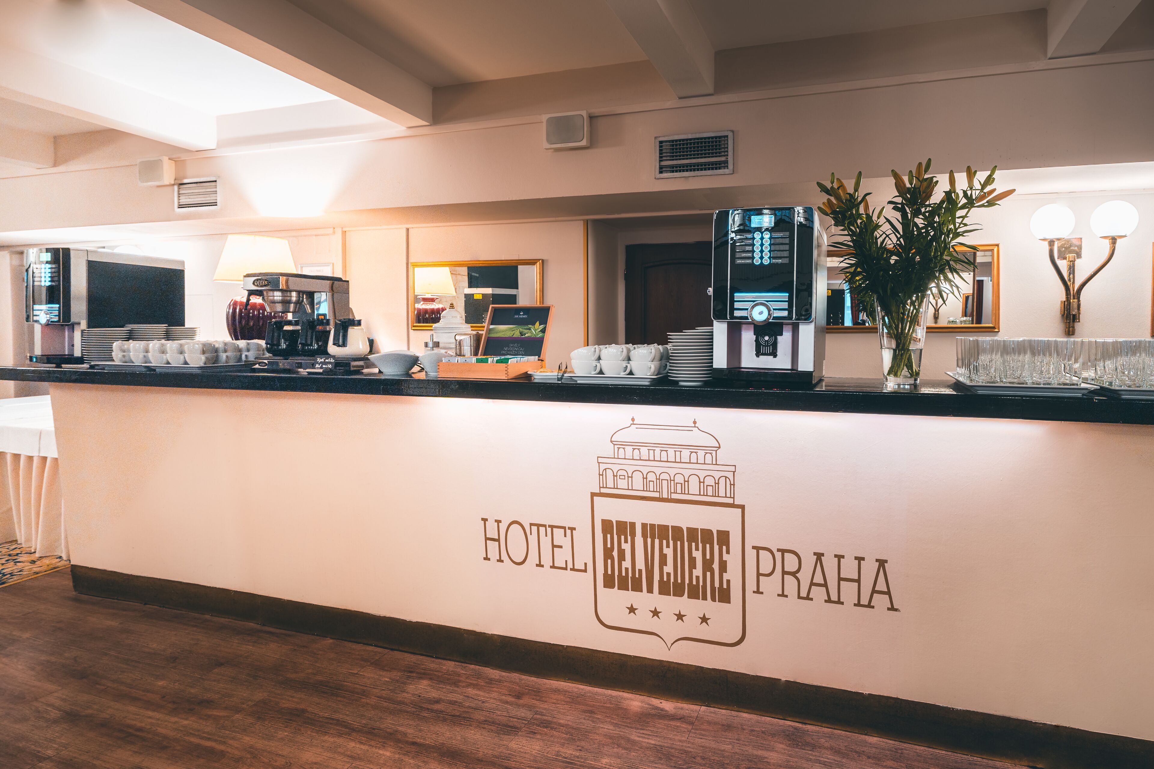 Een receptiebalie in een hotel met een koffieapparaat, een computer en een plant.