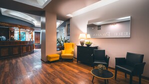 A reception area with a wooden floor, a reception desk, a yellow armchair, and a black leather sofa. - Hotel Belvedere (Prague)