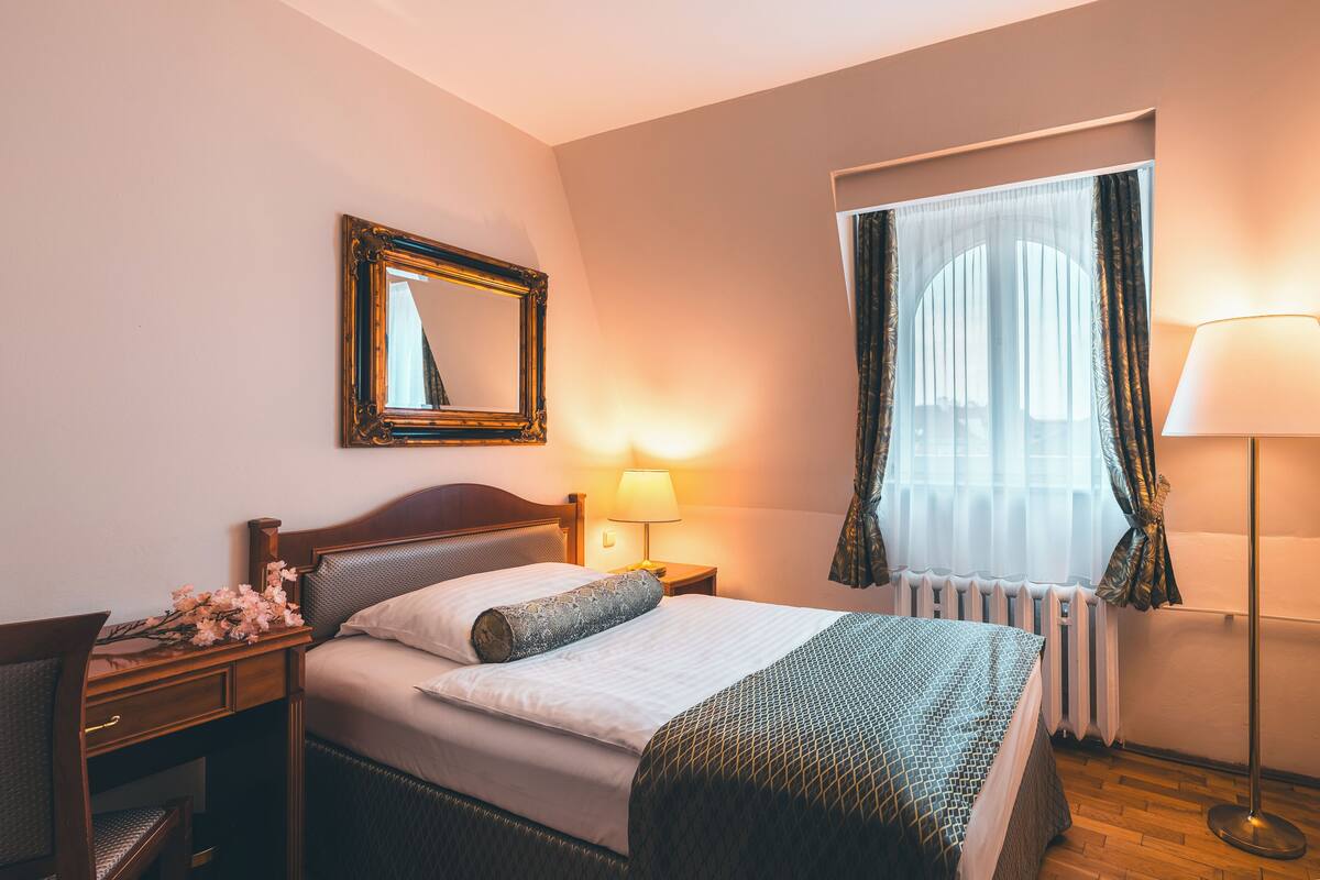 Habitación de hotel con cama, mesita de noche, lámpara y ventana con cortinas.