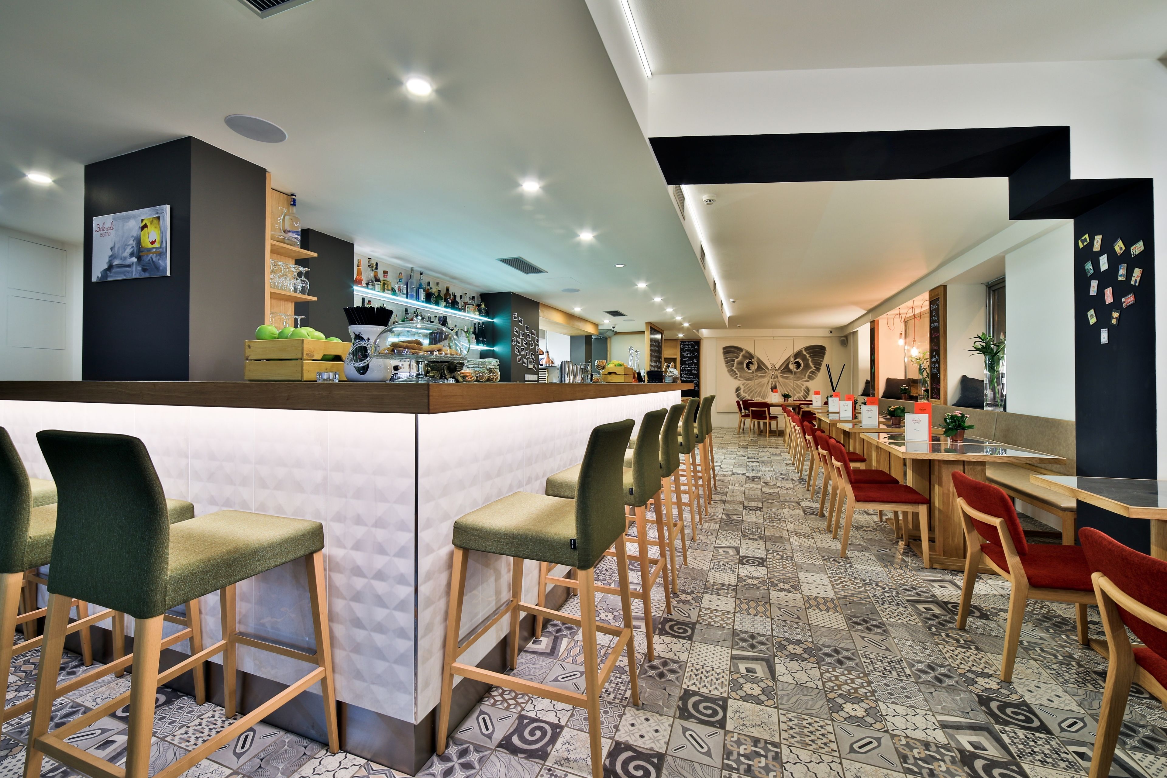 A modern restaurant with a long counter, bar stools, and patterned floor tiles.