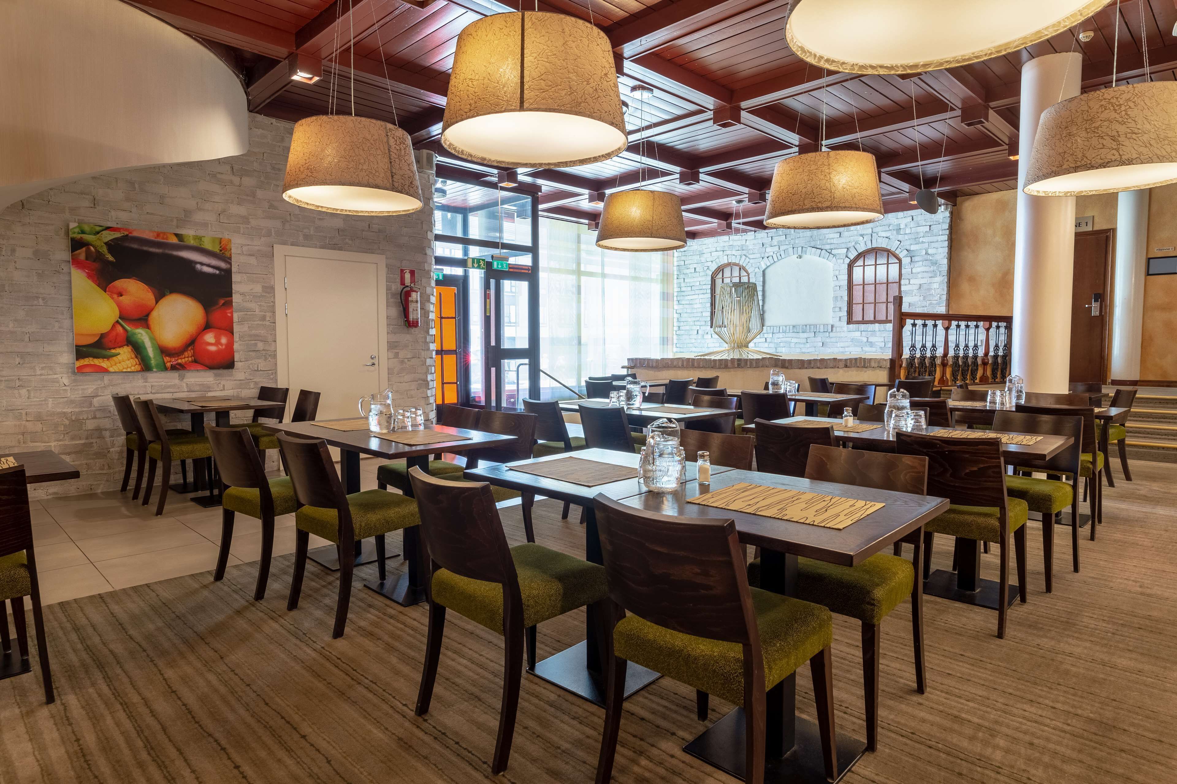 Un restaurant avec des tables et des chaises en bois, des luminaires suspendus et des œuvres d’art murales sur le thème des fruits.