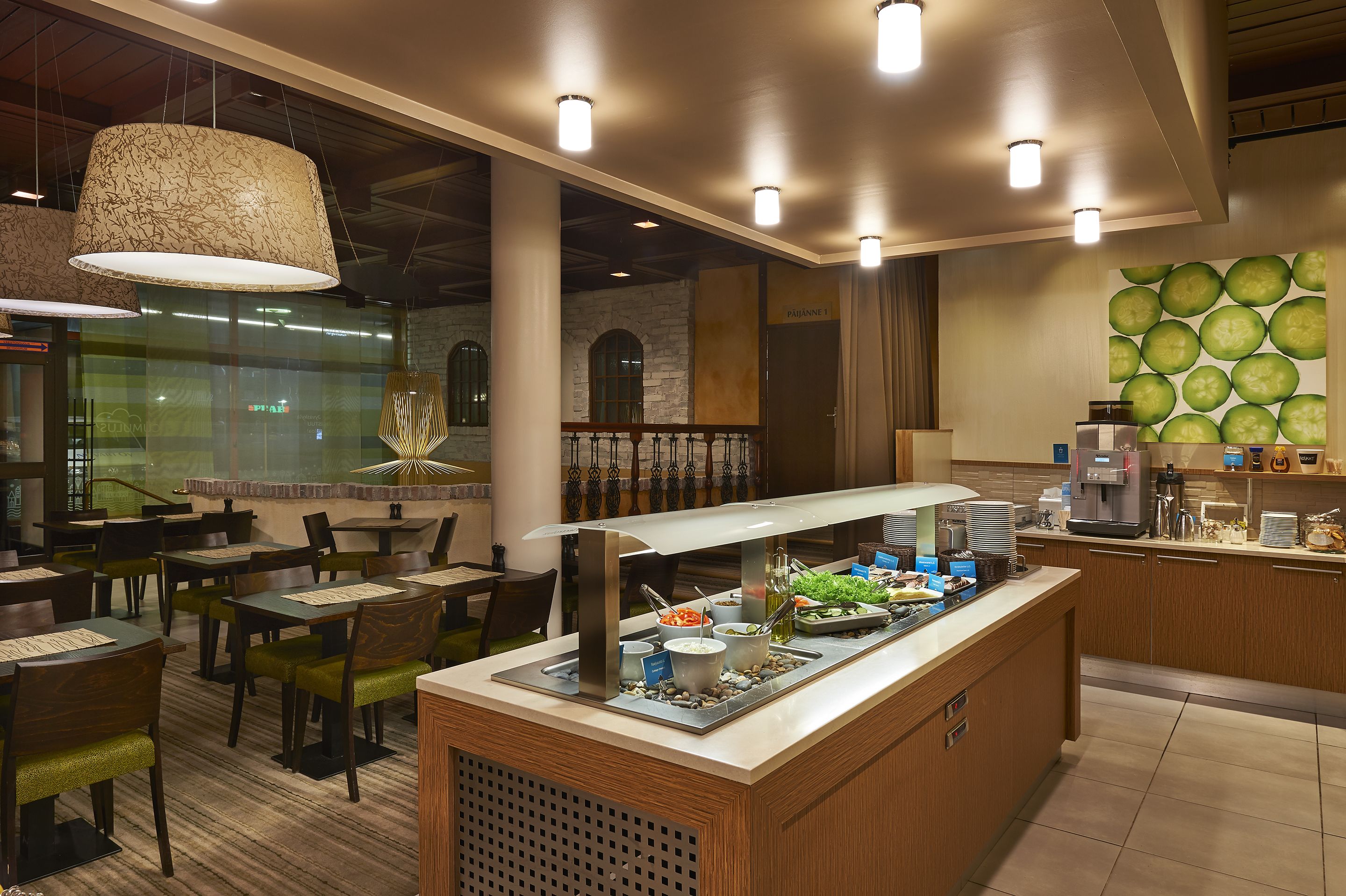 A restaurant with a buffet setup, wooden tables, and hanging pendant lights.