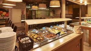 A buffet area with various food options, a seating area with tables and chairs, and a reception desk. - Scandic Jyväskylä City (Jyväskylä)