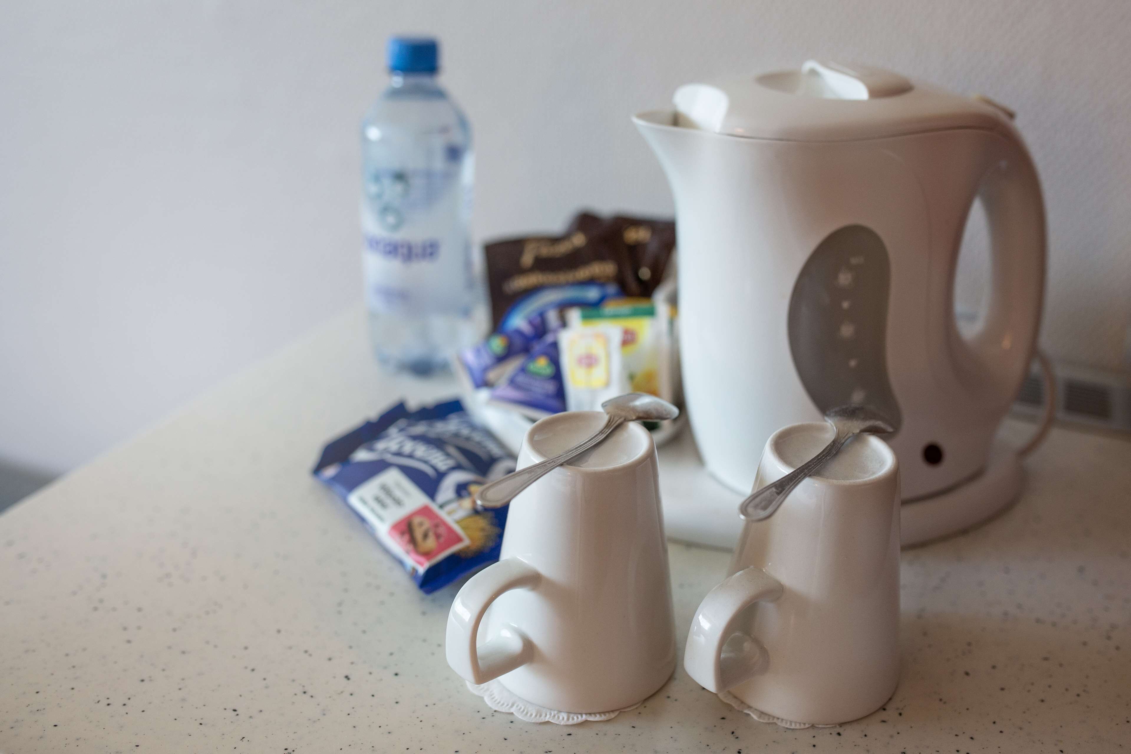 Un taulell de cuina amb una ampolla d'aigua, una cafetera i dues tasses amb cullerades.