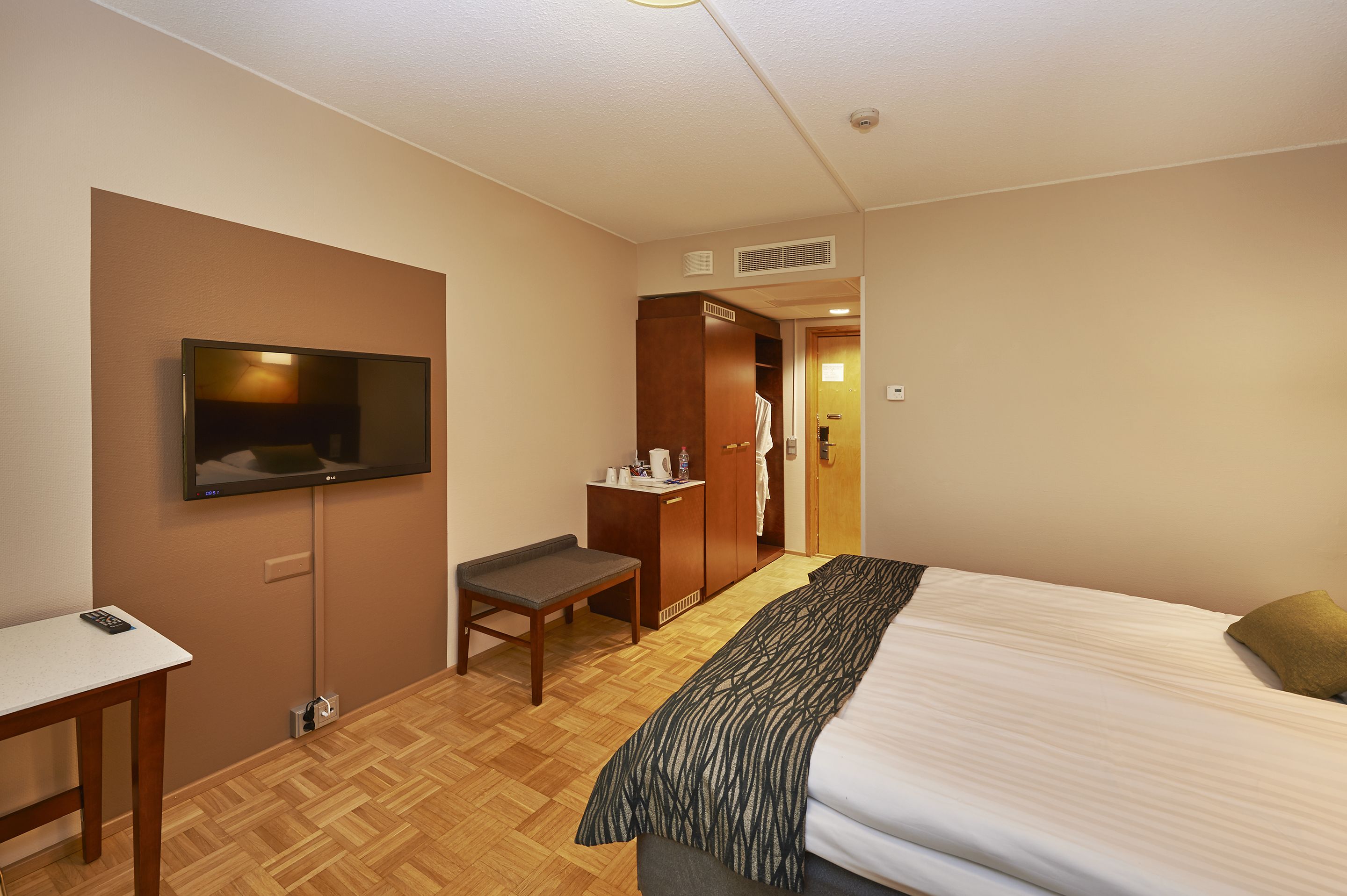 A hotel room with a bed, a desk, a television, a wardrobe, and a bathroom visible through an open door.