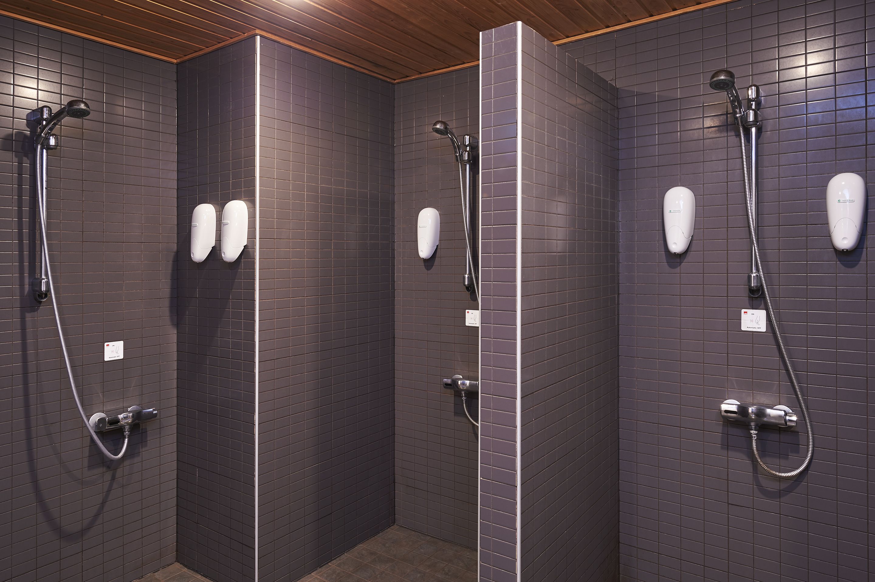 A bathroom with three shower stalls, each equipped with a handheld showerhead and a handheld shower attachment.