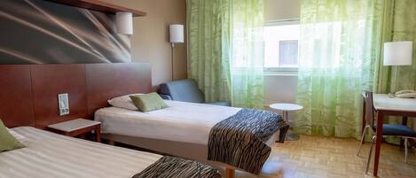 A hotel room with two beds, a desk, a chair, a small table, and a window with green curtains.
