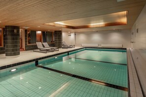 A modern indoor swimming pool with tiled floors and walls, wooden ceiling panels, and two lounge chairs by the poolside. - Scandic Jyväskylä City (Jyväskylä)
