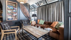 A cozy living area with a wooden coffee table, a brown leather sofa with colorful cushions, a bookshelf with various board games, and a large surfboard decoration. - Scandic Jyväskylä City (Jyväskylä)