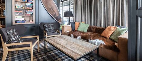 Un espacio de sala acogedor con una mesa de centro de madera, un sofá de cuero marrón con cojines de colores, una estantería con varios juegos de mesa y una decoración de tabla de surf grande.